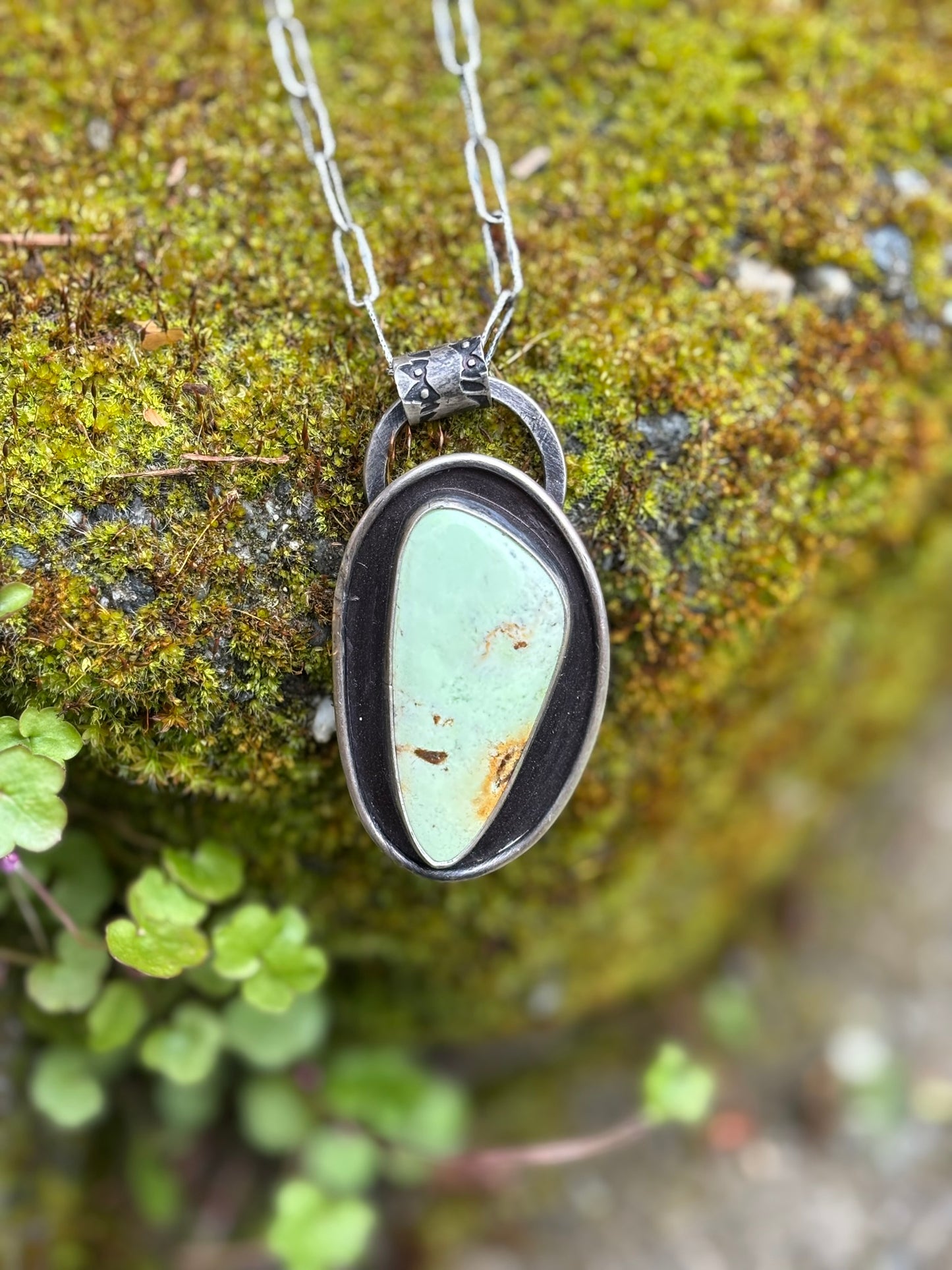 handmade citron magnesite pendant with stamped bail and dark patina background with wire frame. shown on a mossy rock background