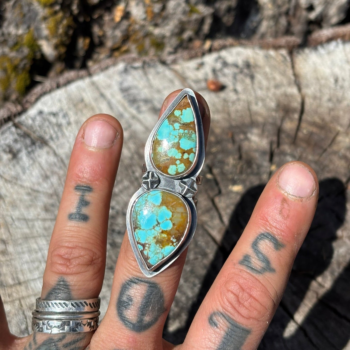 2 teardrop turquoise stones set in fine and sterling silver with 2 star shaped silver shots worn on a tattooed hand