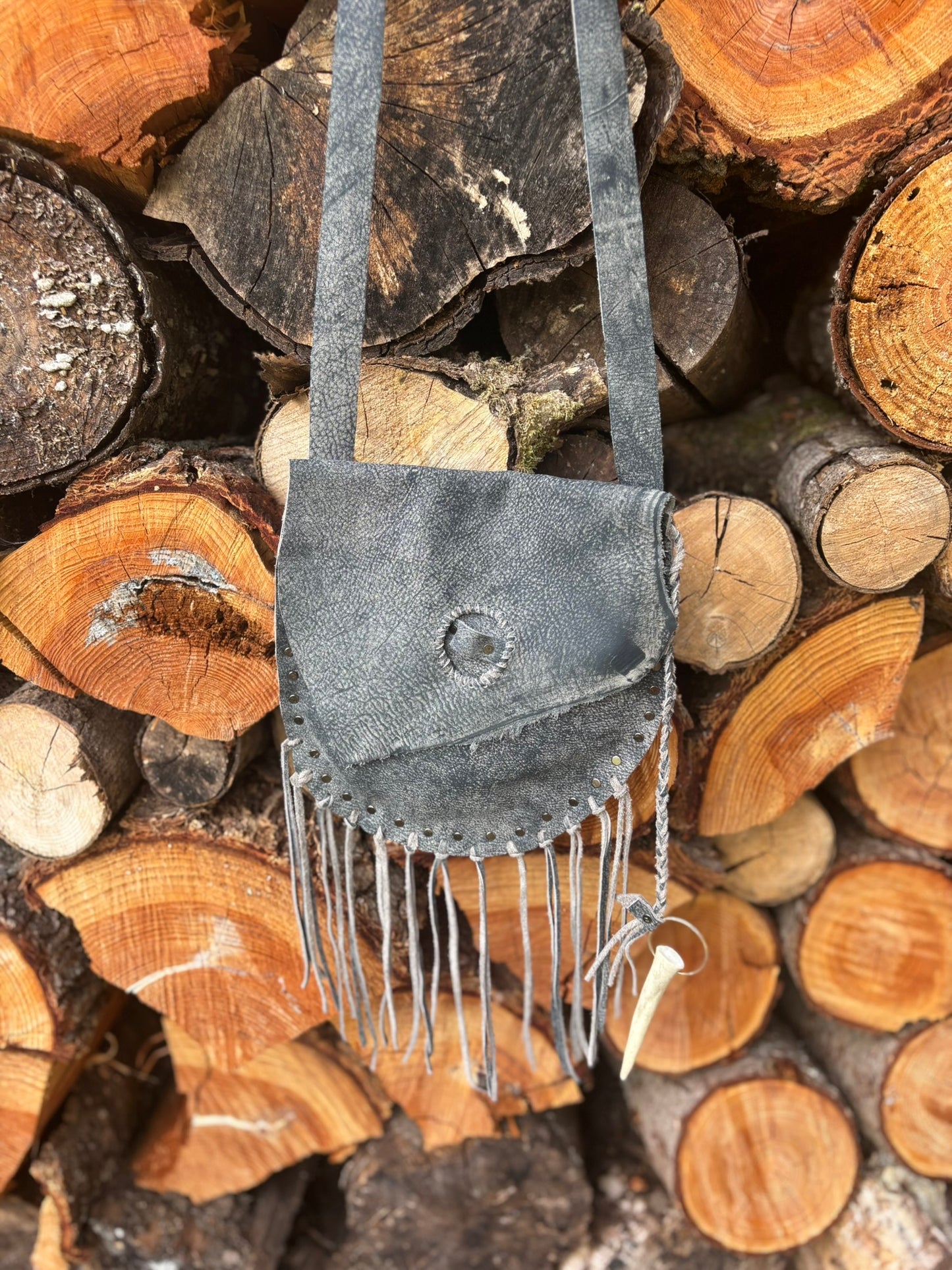 Gray suede handbag with fringe on a stack of wooden logs