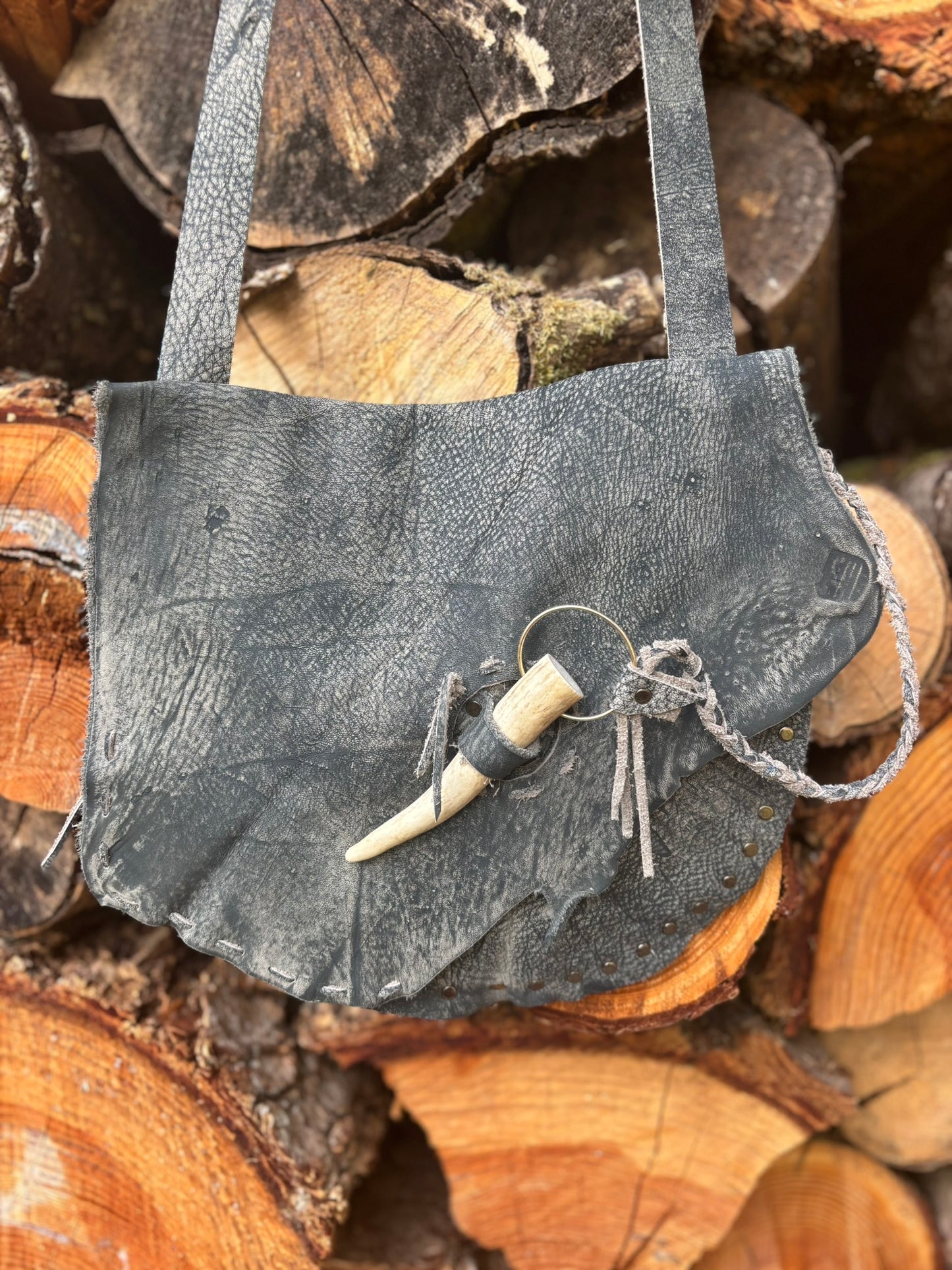 Small dark gray leather bag with a keychain on a stack of wooden logs
