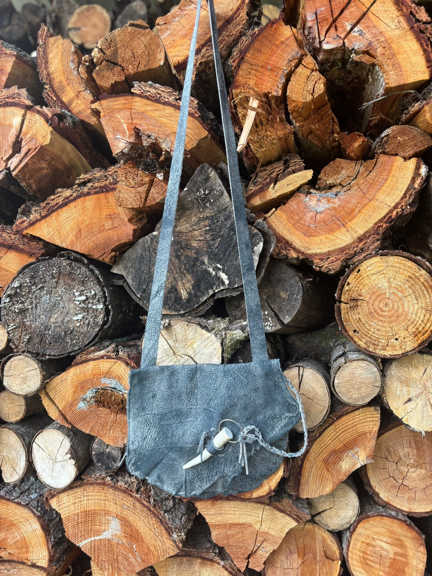 Small gray bag hanging on a stack of wooden logs