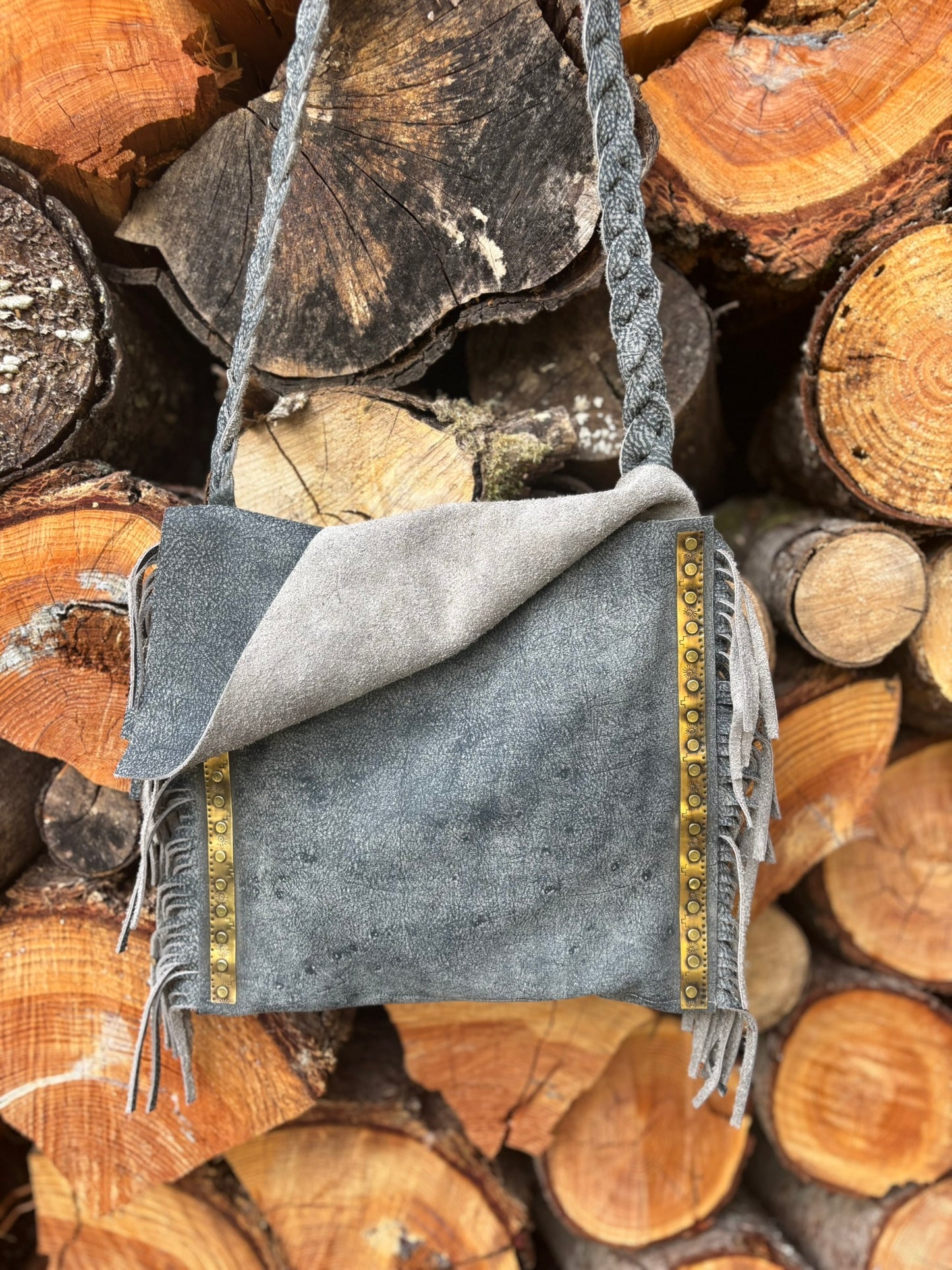 Gray suede handbag with gold accents on a stack of wooden logs