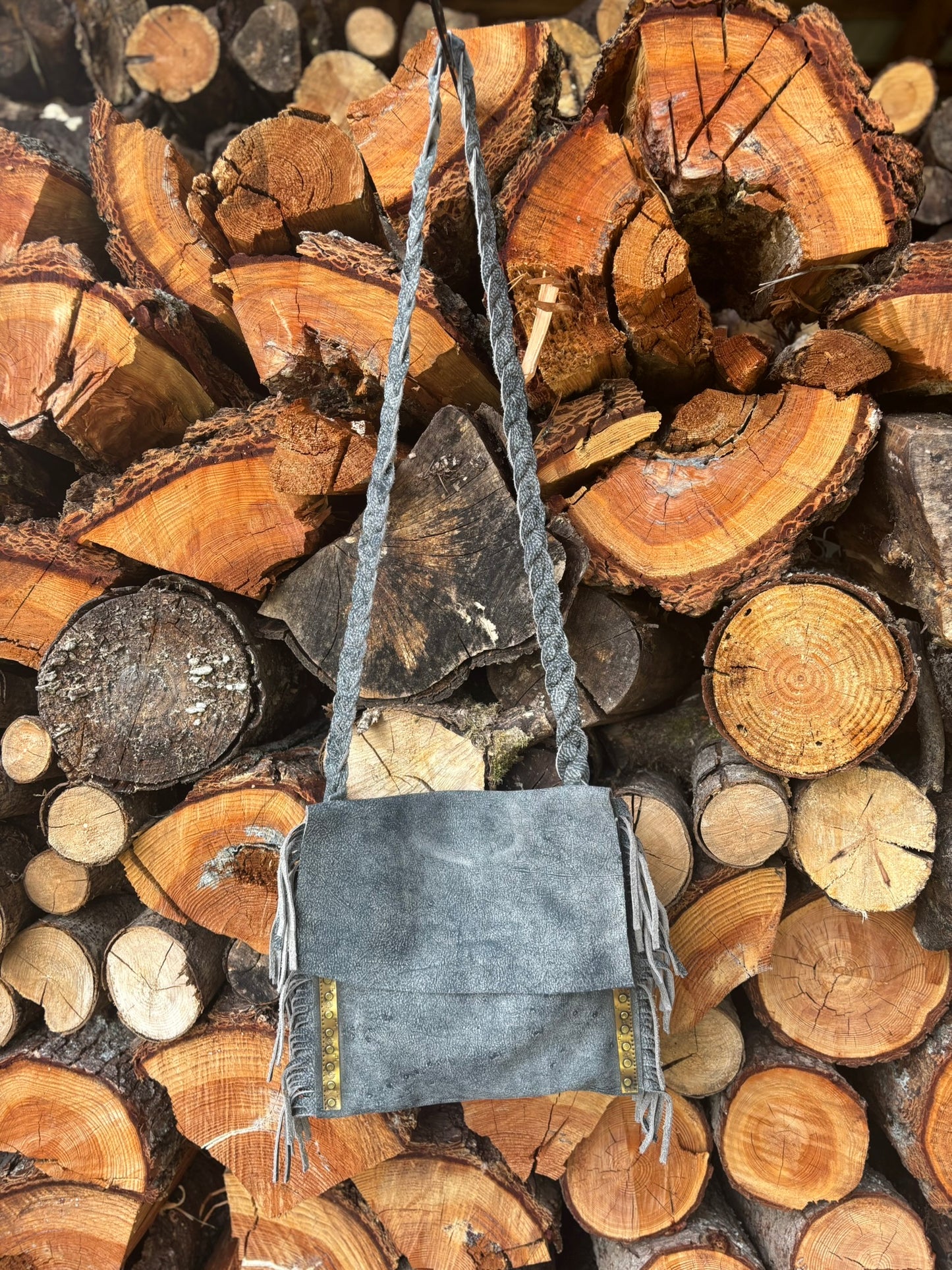 Gray handbag with a strap on a background of stacked wooden logs