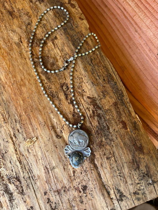 handmade buffalo and variscite pendant with silver shots and hand stamped wings on a silver ball chain on a piece of fire wood