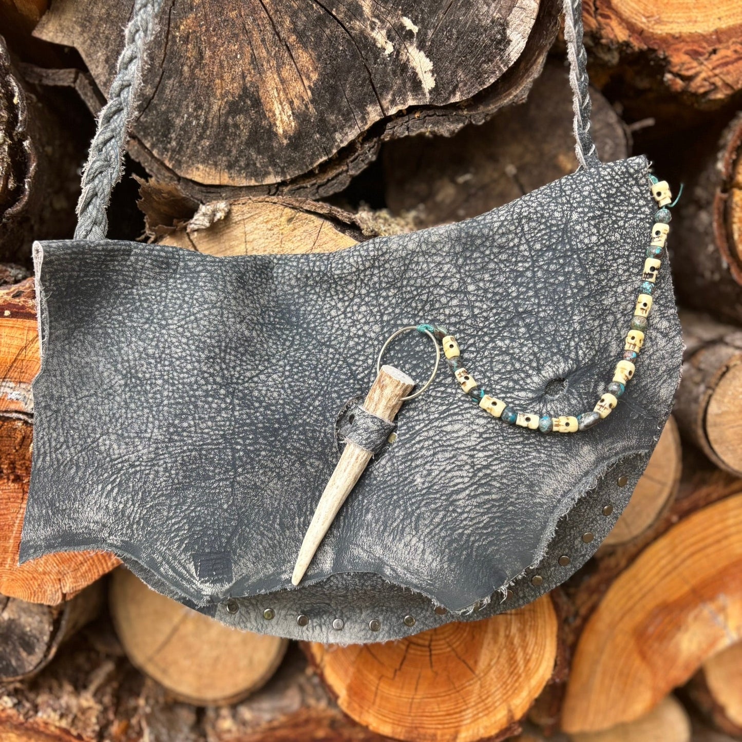 Gray leather handbag with decorative elements on a stack of wooden logs