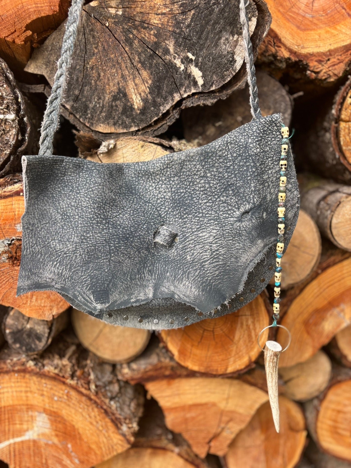 Dark gray leather bag with decorative elements on a background of stacked wooden logs