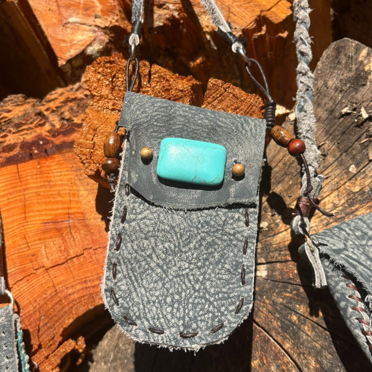 Gray leather pouch with a turquoise stone on a wooden surface