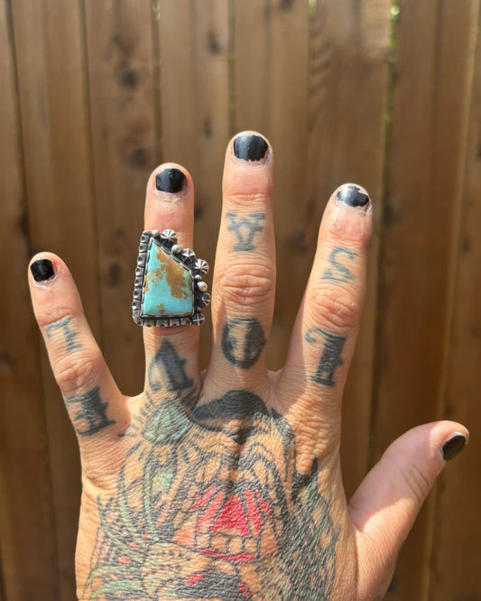 handmade turquoise ring with lots of silver shots and stars and stamped heavy border worn on ring finger of tattooed hand