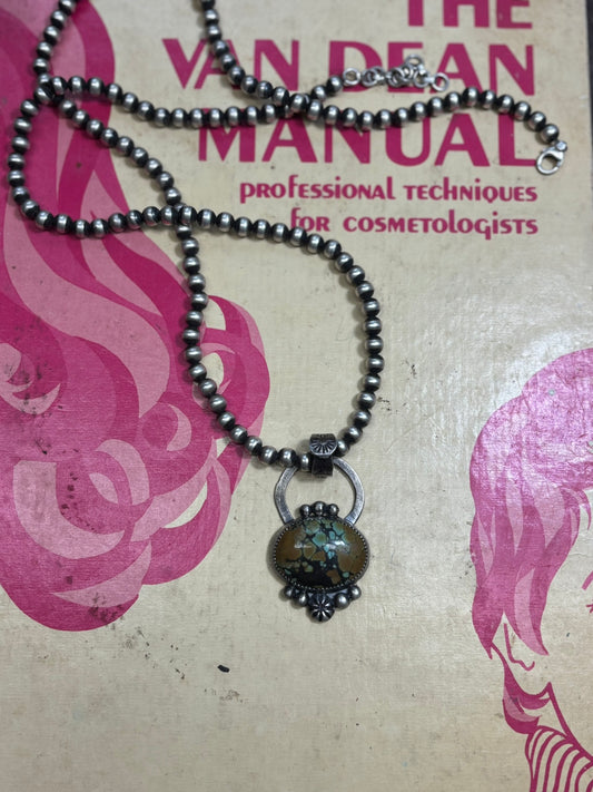 turquoise handmade pendant on string of navajo pearls on a book