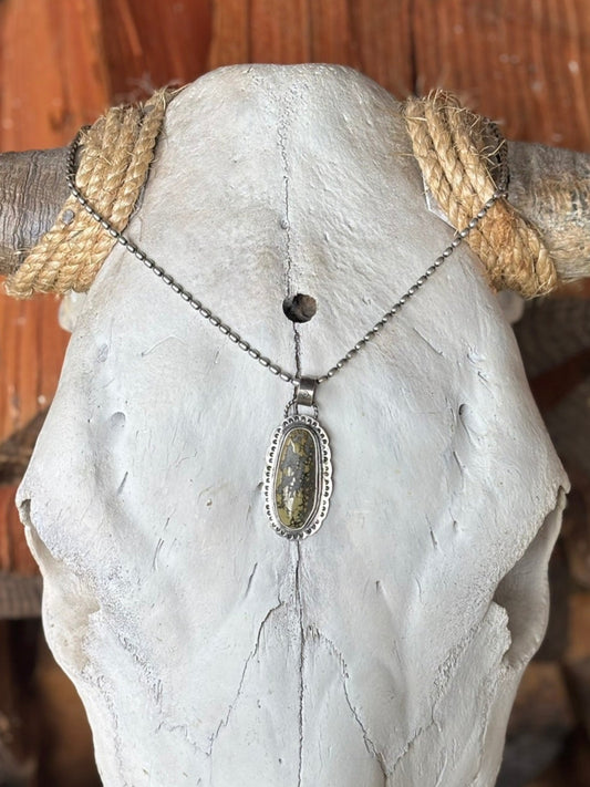 large variscite stone set in 2 layers of silver bezel wire hand stamped on a handstamped backplate with artist sign and leaf stamp on backside. hung on silver ball chain draped on bull skull