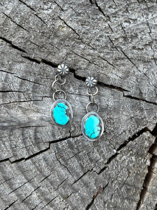 handmade silversmith high quality turquoise earrings with silver shot post and chain dangle shown on wood round backdrop
