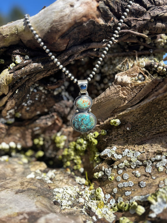 handmade pendant with 3 stones. 2 large turquoise and one blue star sapphire stone on the bail on a string of 6mm navajo pearls. hanging from a driftwood log with barnacles