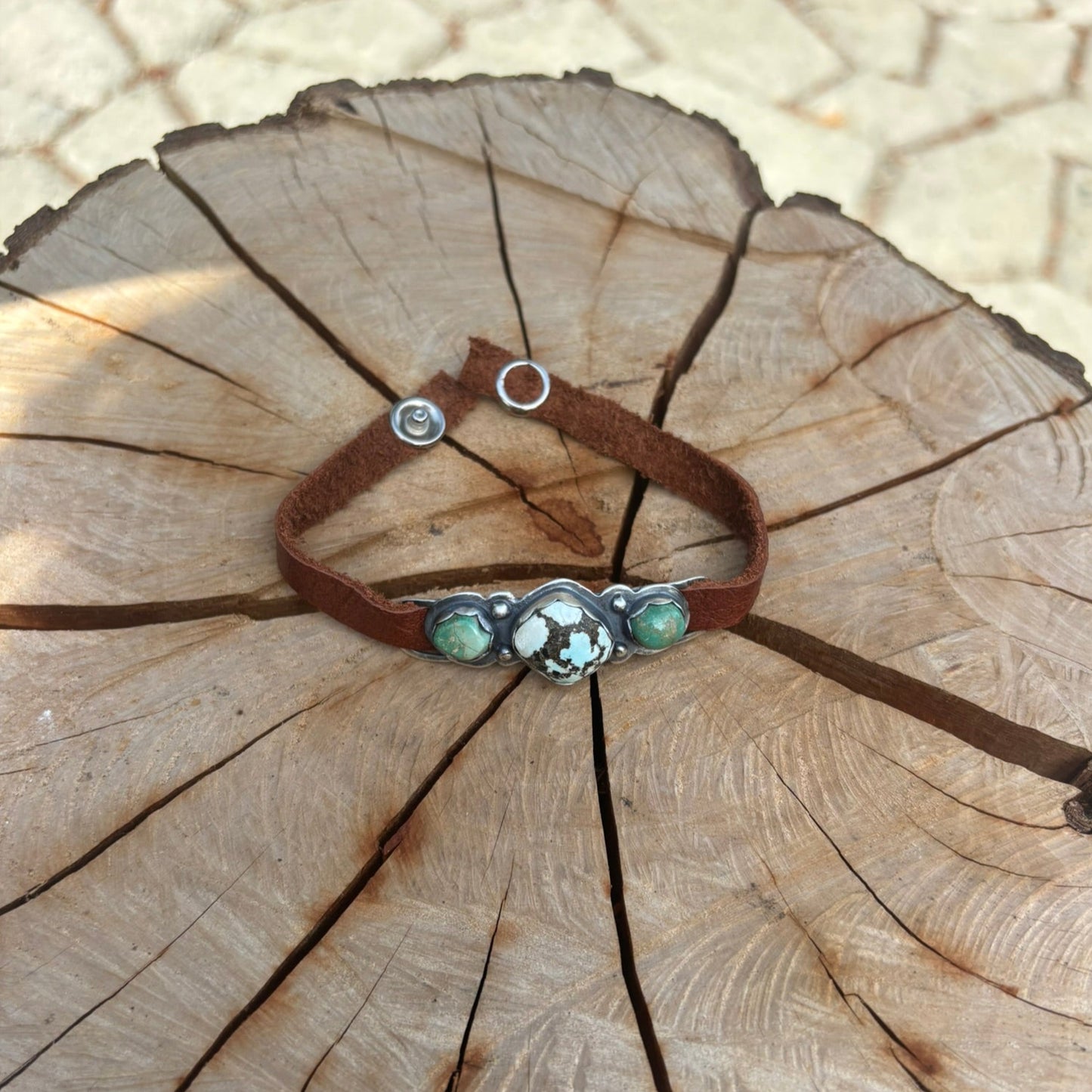 Bracelet with green stones and brown leather strap on a wooden stump