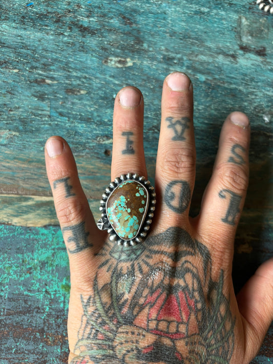 large turquoise ring with large silver bead wire and star shot details on left finger of right hand with tiger tattoo
