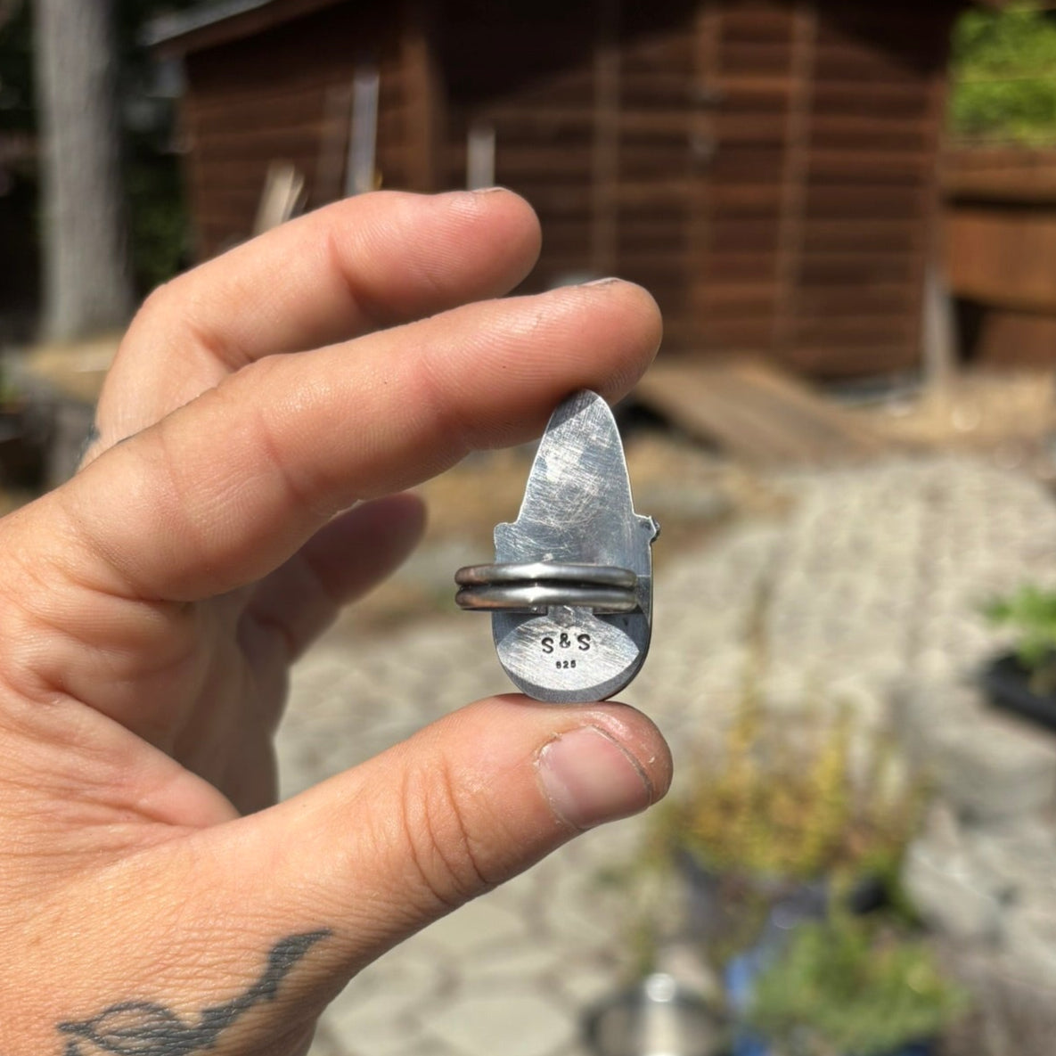 hand holding siler ring back side view showing artist stamp, outdoors