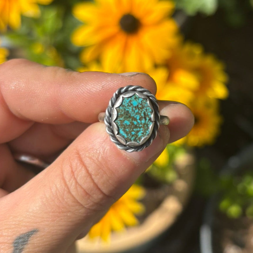 Hand holding a ring with a green stone in front of potted plants