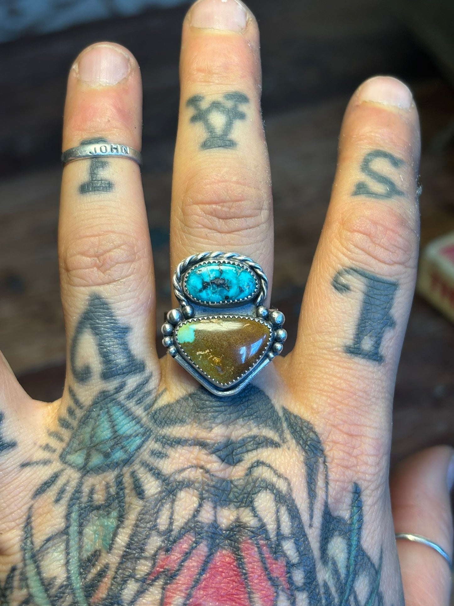 Hand with tattoos wearing a ring with turquoise and amber stones.
