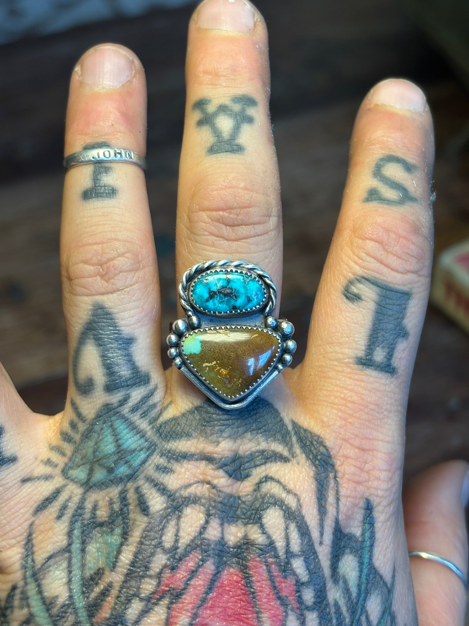 Hand with tattoos wearing a ring with turquoise and amber stones.