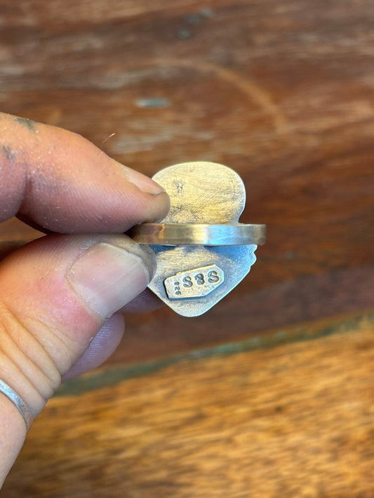 Silver ring with engraved text held by a hand against a wooden background