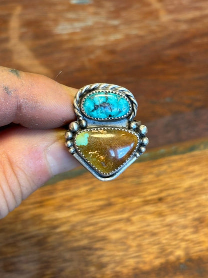 Ring with turquoise and amber stones held by a hand on a wooden surface