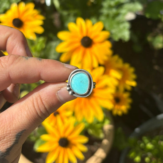 Hand holding a turquoise ring with yellow flowers in the background