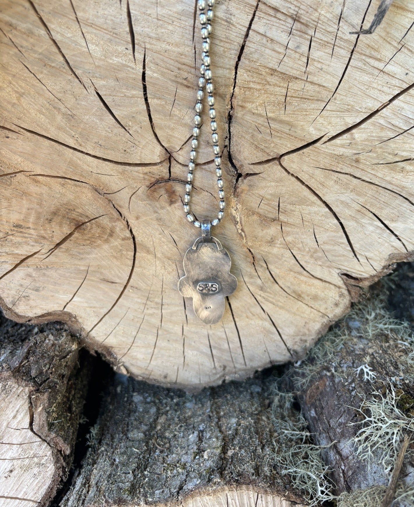 backside view of handmade buffalo nickel and turquoise pendant on silver ball chain hung on the end of a wood round