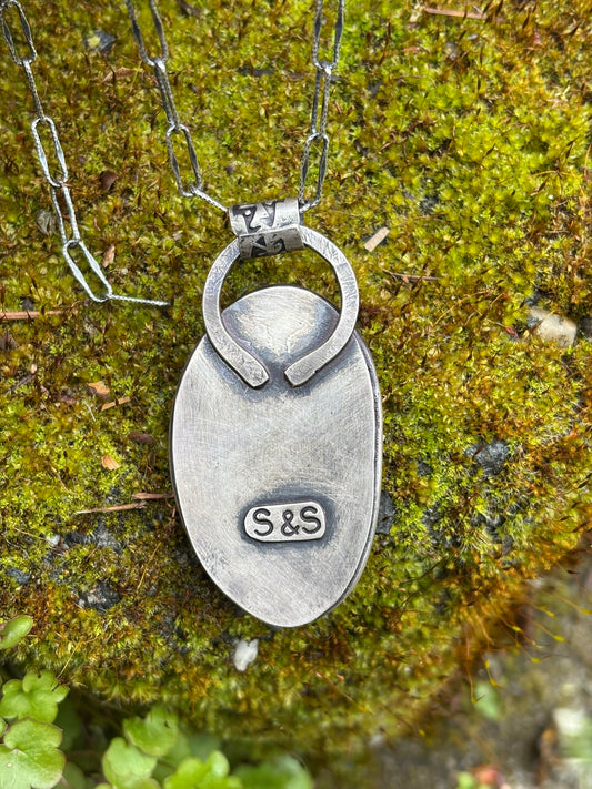 back side of handmade citron magnesite pendant showing artists stamp signature, laid on mossy rock, shown with chain (not included)