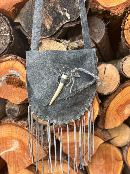 Gray suede handbag with fringes on a background of stacked wooden logs