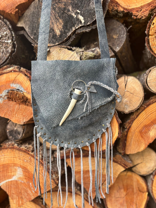 Gray suede handbag with fringes on a background of stacked wooden logs
