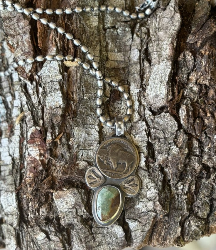handmade buffalo nickel and turquoise pendant shown on silver ball chain laying on a piece of wood bark