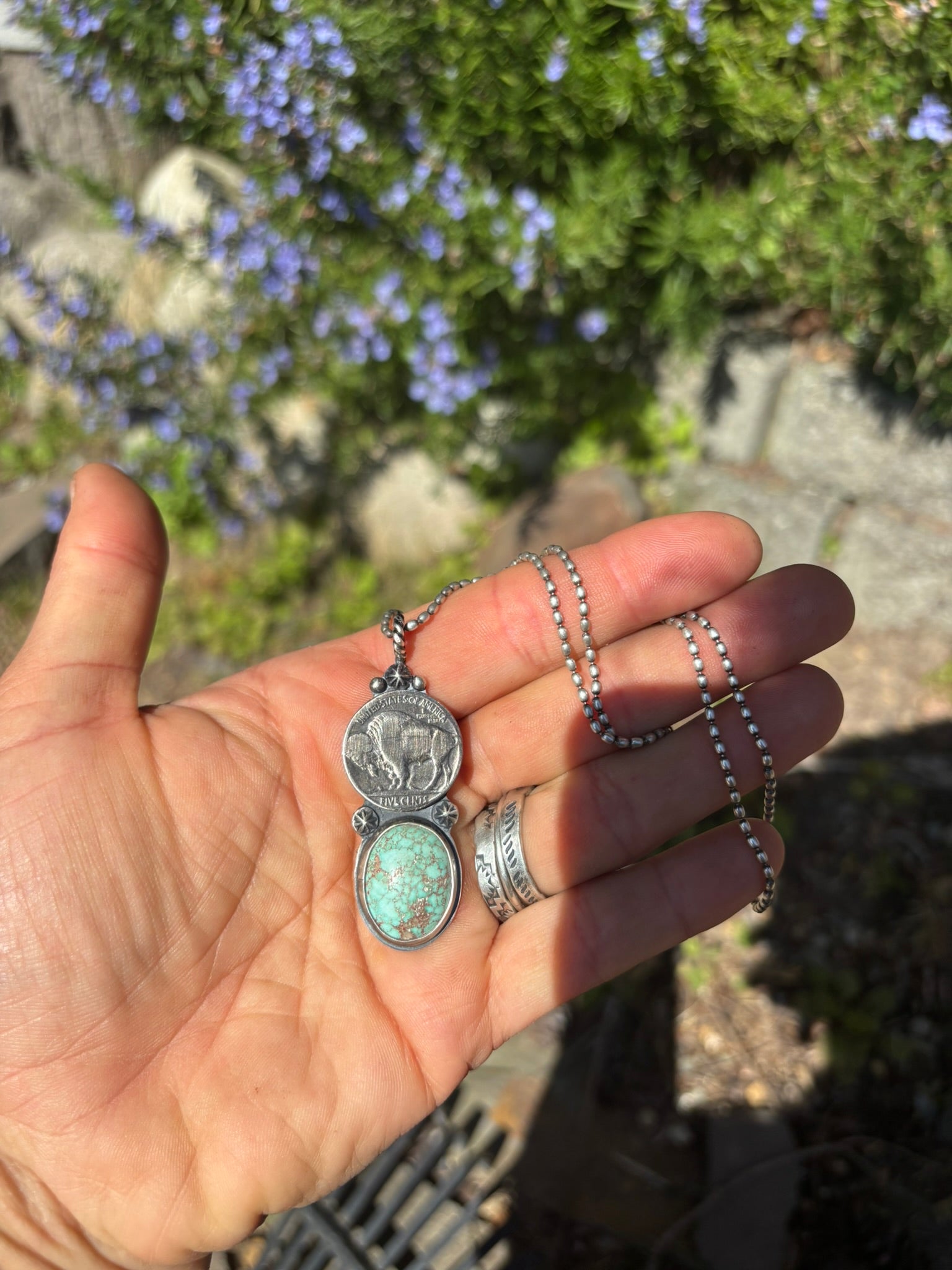 bufflao nickel and turquoise pendant with silver shot details on a silver ball chain in palp of hand with garden backdrop
