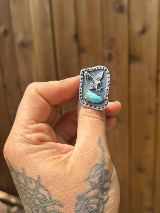 handmade ring featuring a cast eagle and turquoise stone with a hammered stamped border and a dark patina black background
