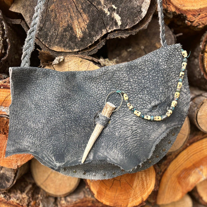 Gray leather handbag with decorative elements on a stack of wooden logs
