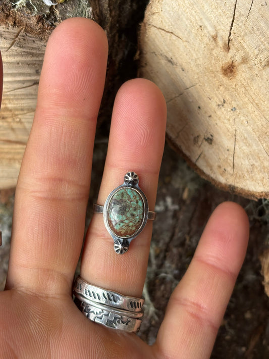turquoise ring with 2 star shots on inside of ring finger in front of a wood background
