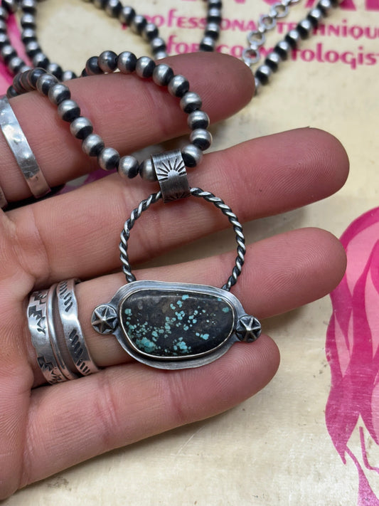 handmade turquoise and silver pendant with silver shots, twist wire detail and hand stamped bail on a navajo pearl chain held by artist hand
