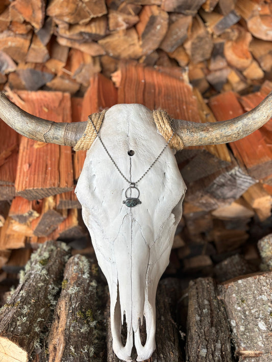 handmade turquoise and silver pendant with silver shots and twist wire details and large hand stamped bail hanging on silver ball chain draped over bull skull in wood stack backdeop