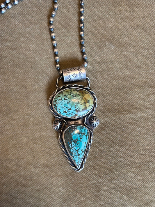 Turquoise stone pendant on a chain against a beige background