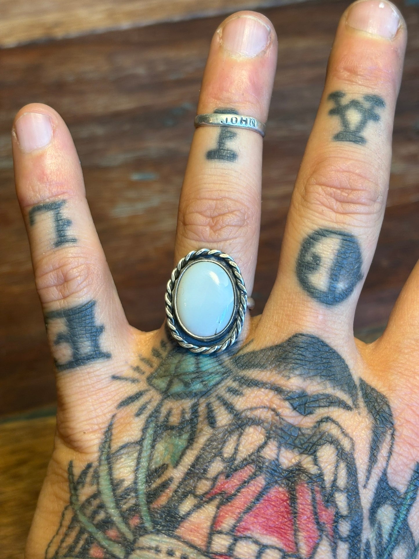 Hand with tattoos wearing a ring with a blue stone on a wooden surface