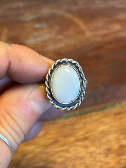 Silver ring with a white stone held by a hand on a wooden surface