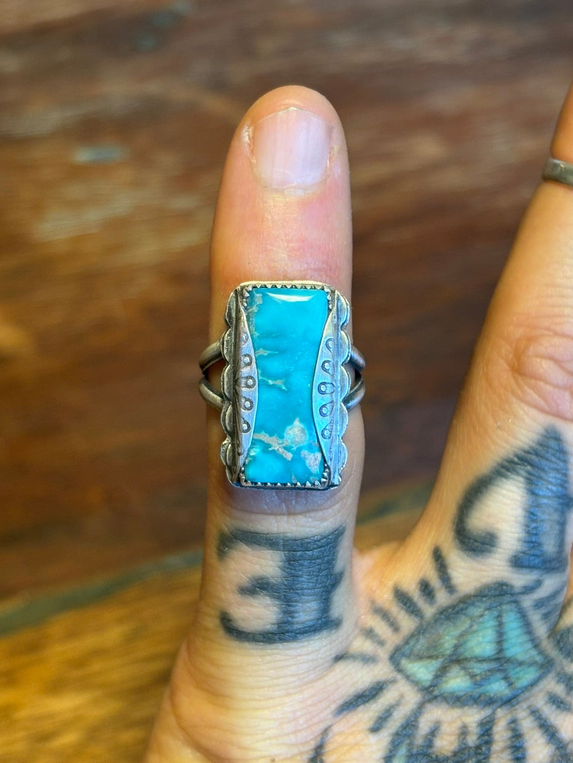 Hand wearing a turquoise ring with intricate design on a wooden surface