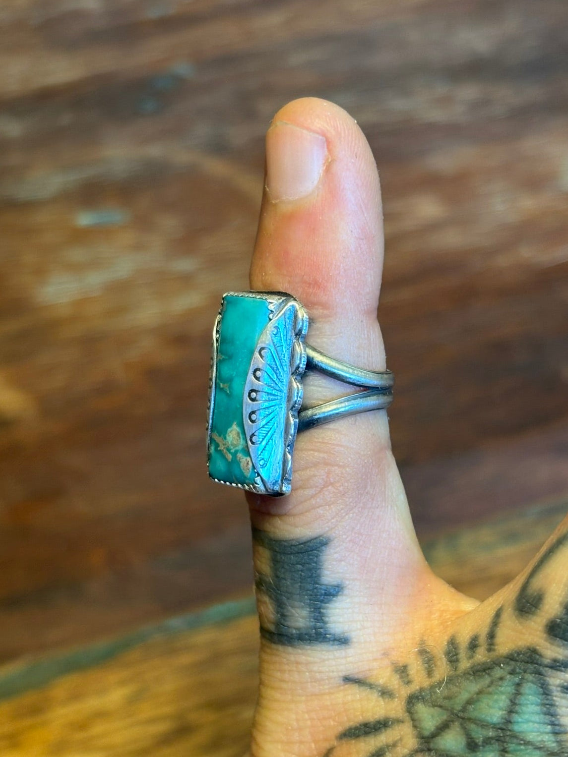 Hand wearing a turquoise ring on a wooden surface