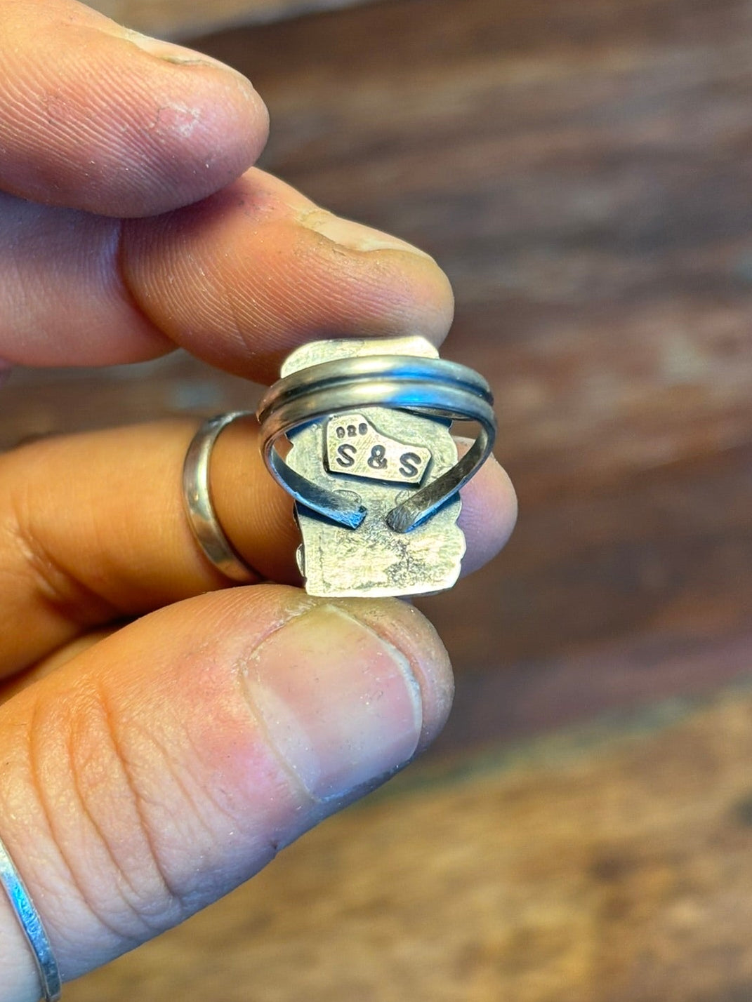 Silver ring with 'S & S' engraving held in a hand against a wooden background