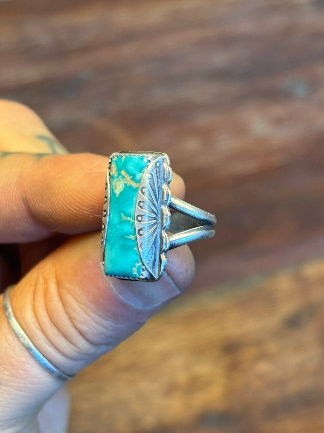 Turquoise ring with silver band held in a hand against a wooden background