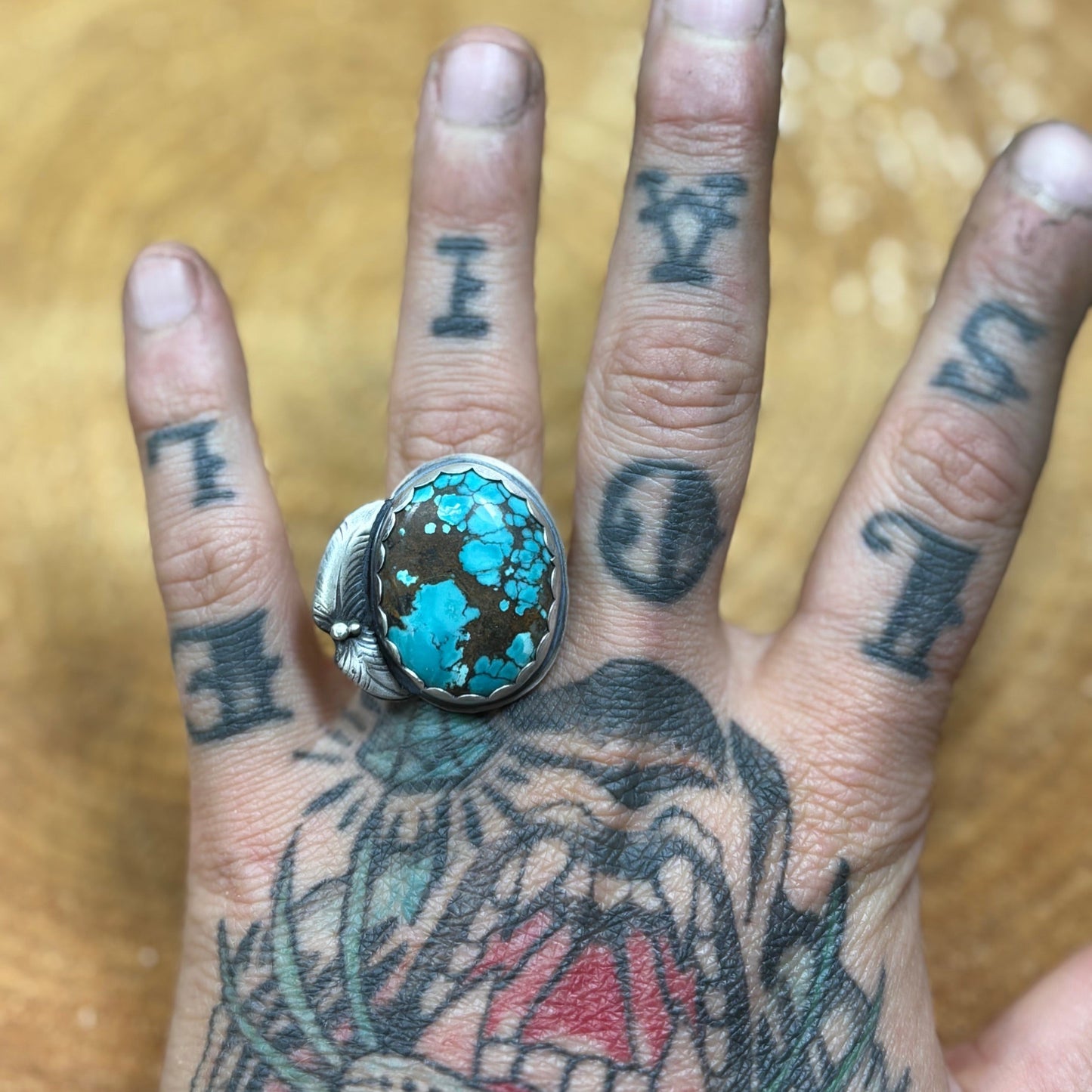 silver and turquoise ring with scalloped bezel and 2 feathers on a tattooed hand over a wood round. handmade sterling and fine silver ooak