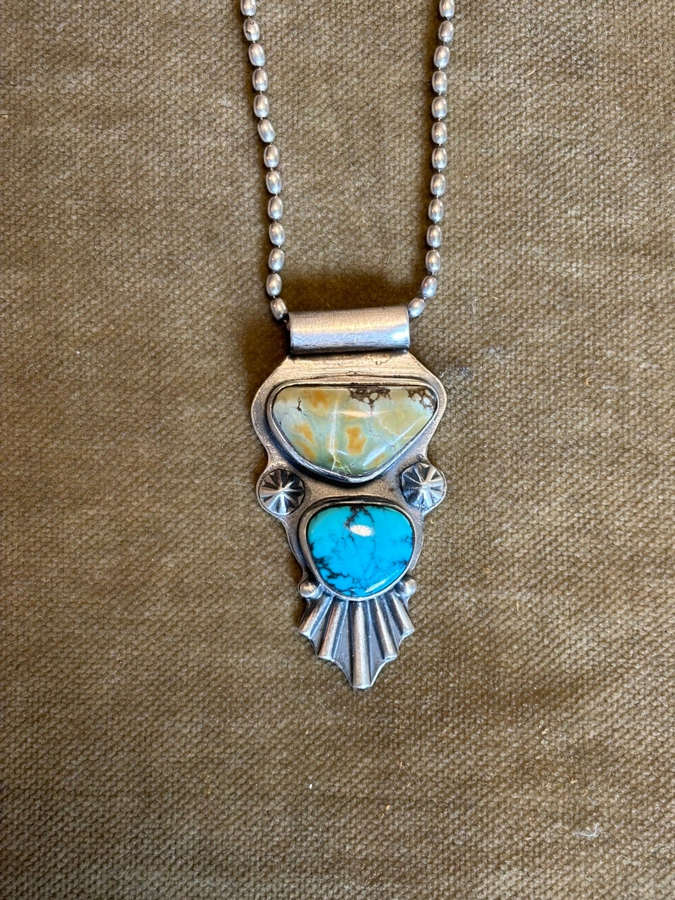 Silver necklace with a turquoise pendant on a beige fabric background