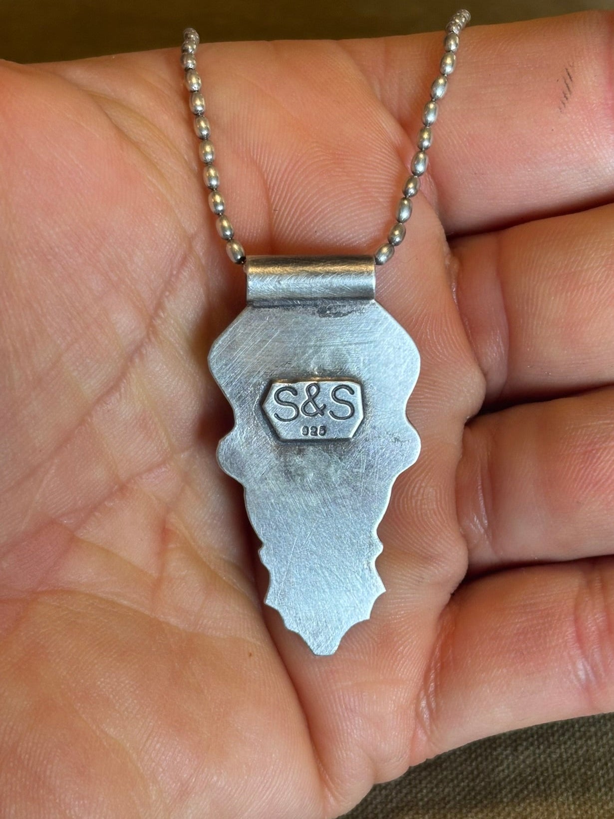 Silver key-shaped pendant with 'S&S' initials held in a hand.