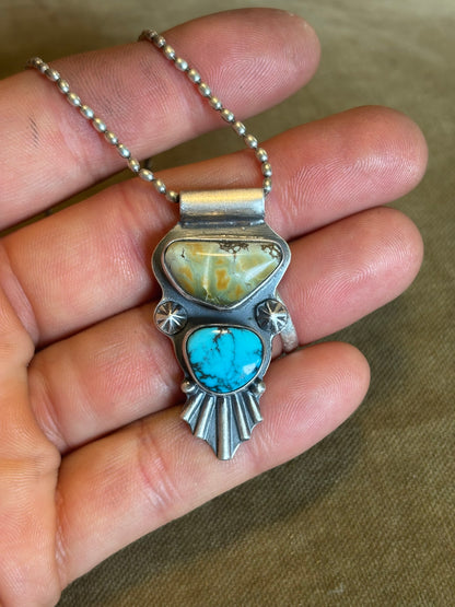 Silver pendant with turquoise stone held between fingers on a neutral background