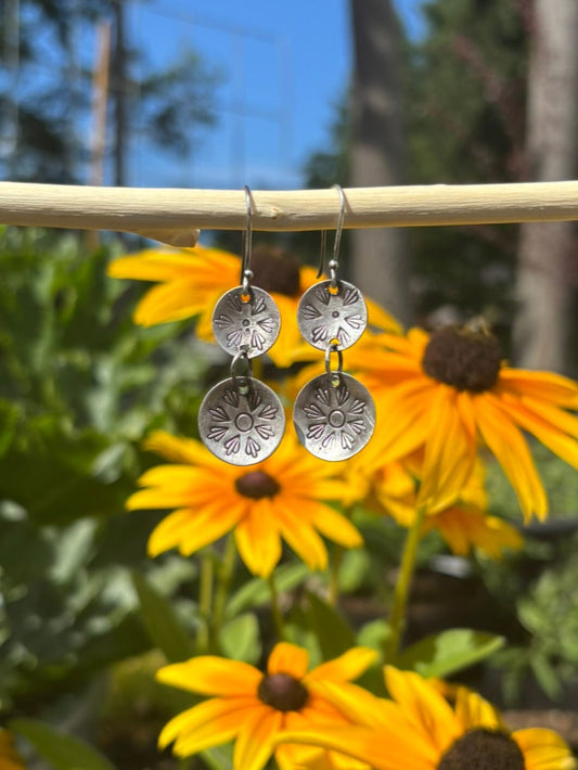 Silver earrings hanging from a branch with yellow flowers and green leaves in the background.