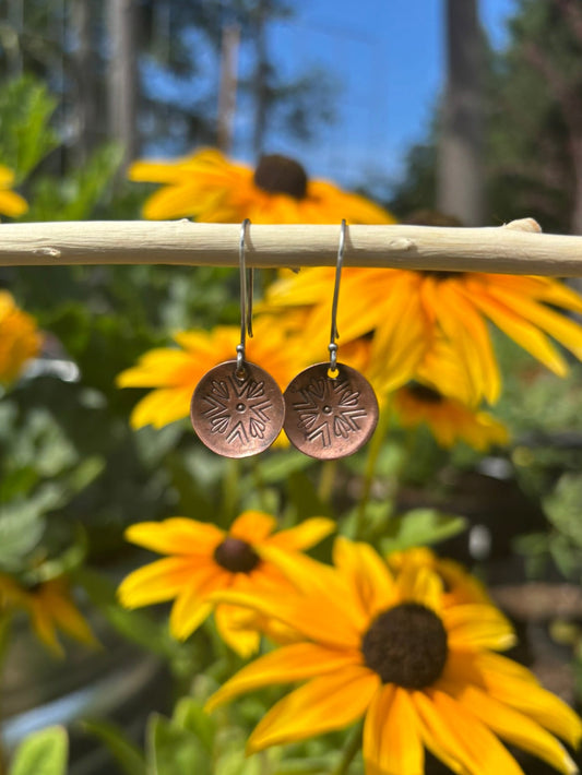 Bronze earrings on a stick with yellow flowers in the background