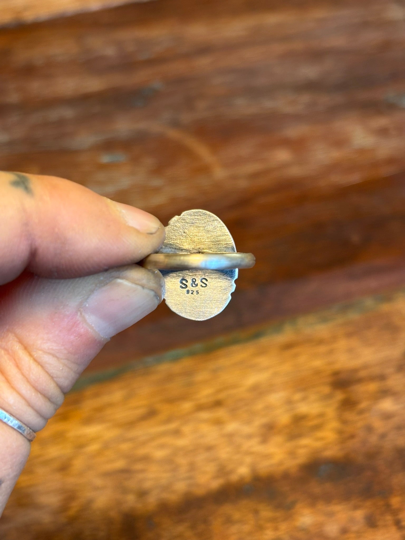 Small gold ring with 'S&S' engraving held by a hand against a wooden background